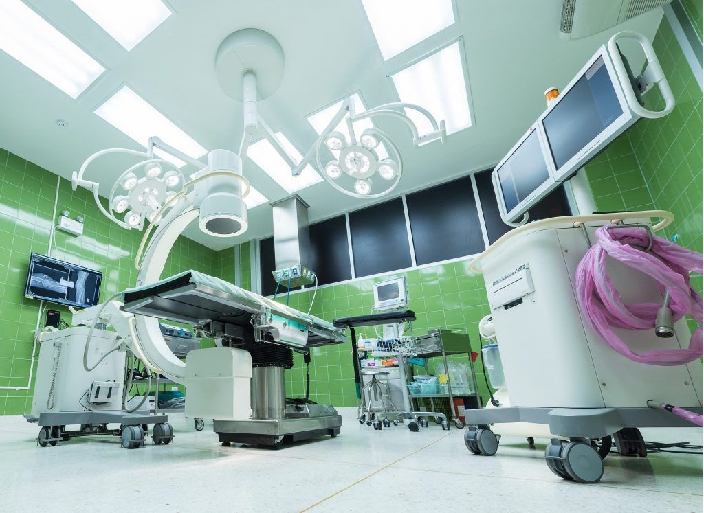 An empty operating room in a hospital with a surgical table and monitors.