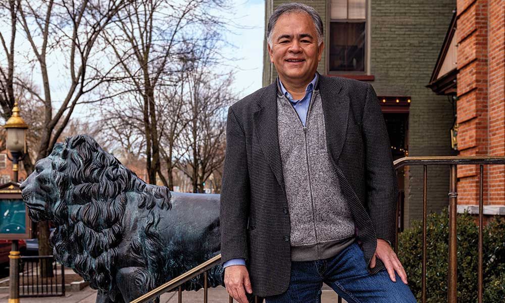 A man is sitting on a railing next to a statue of a lion.