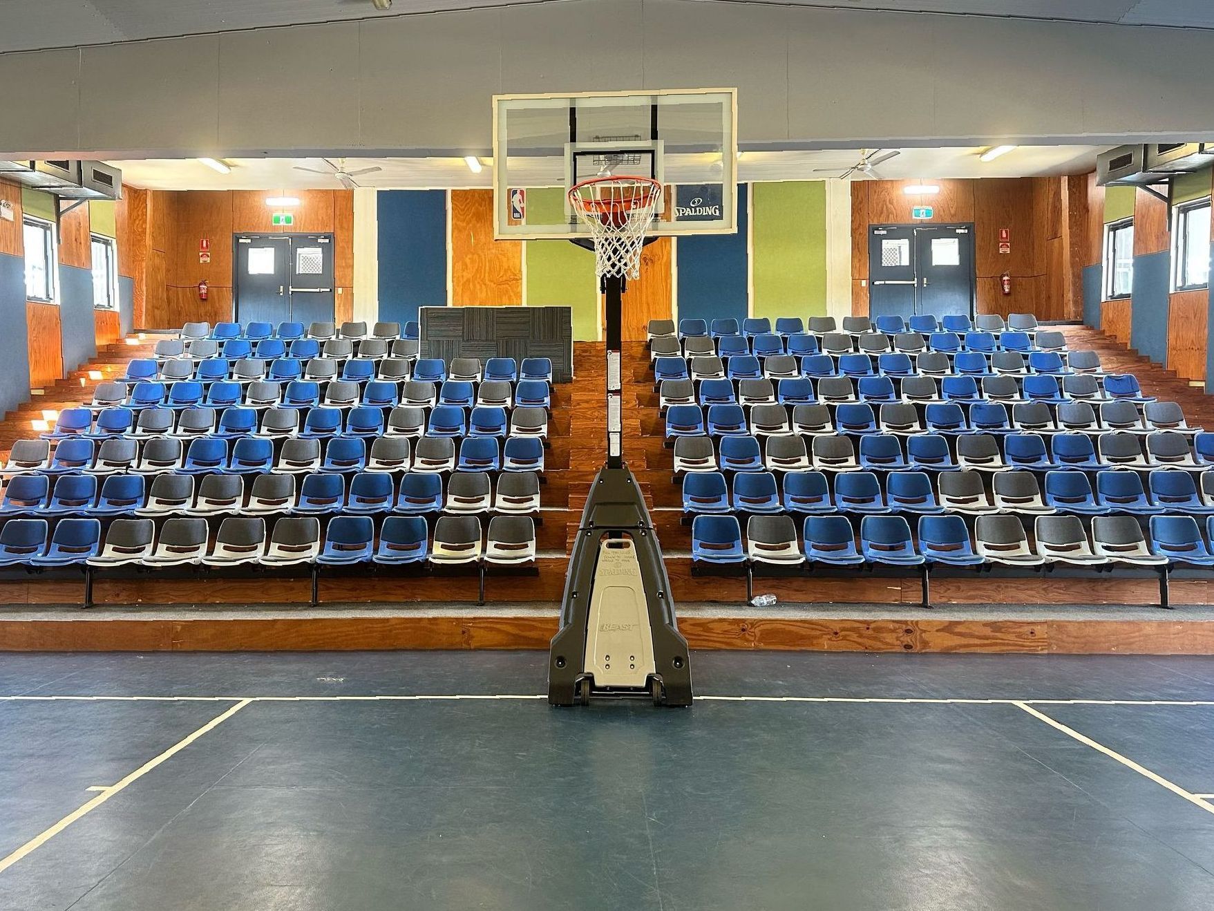 A basketball hoop in a gym with rows of blue seats