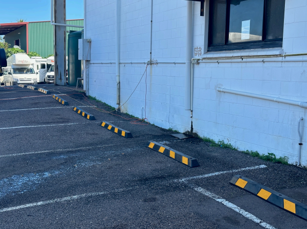 A car park with wheel stops and a white building in the background