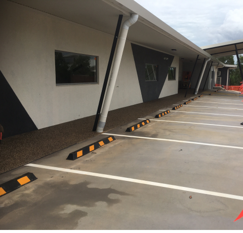 A car park with wheel stops and a building in the background