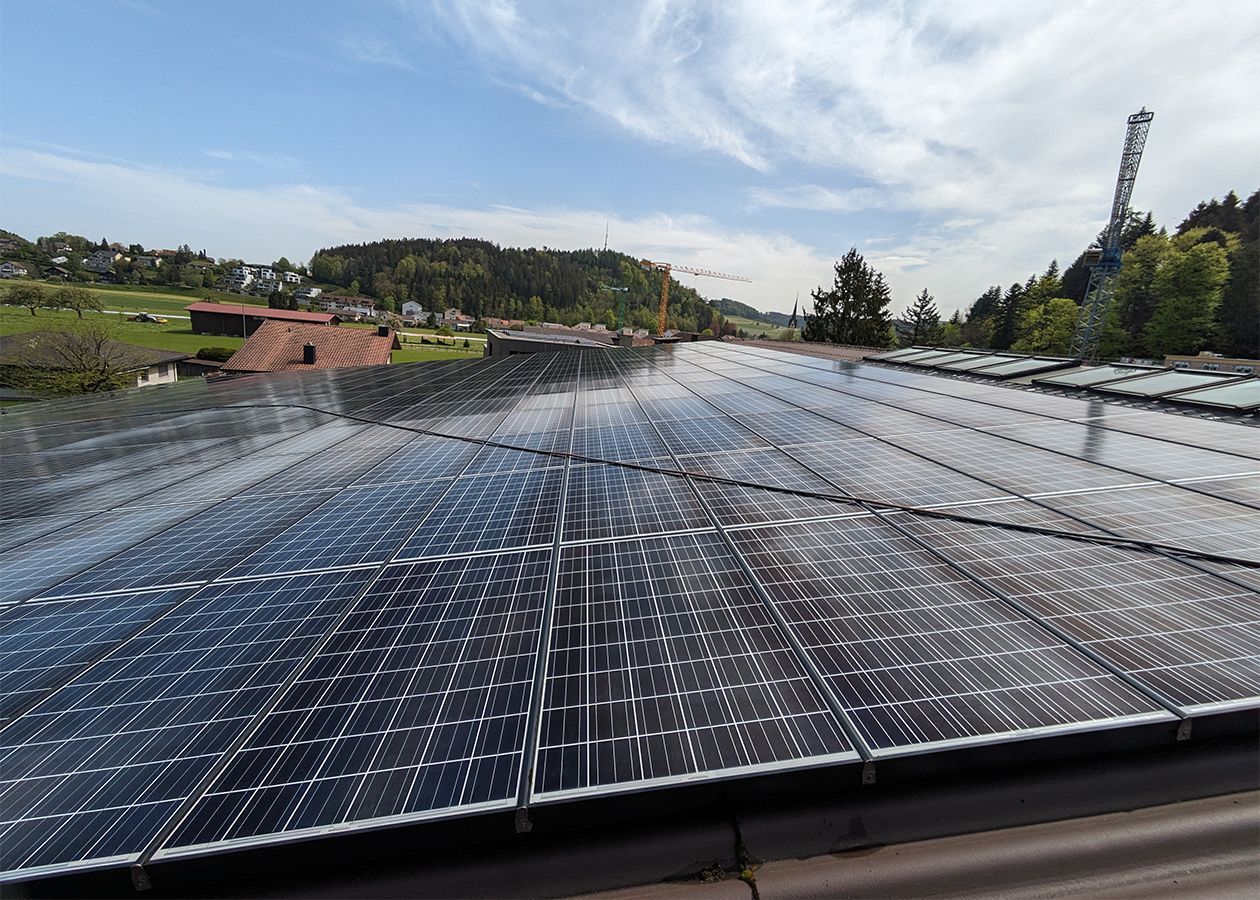 Solarpaneele auf einem Gebäudedach, die den Himmel und die umliegende Landschaft reflektieren, sonniger Tag.