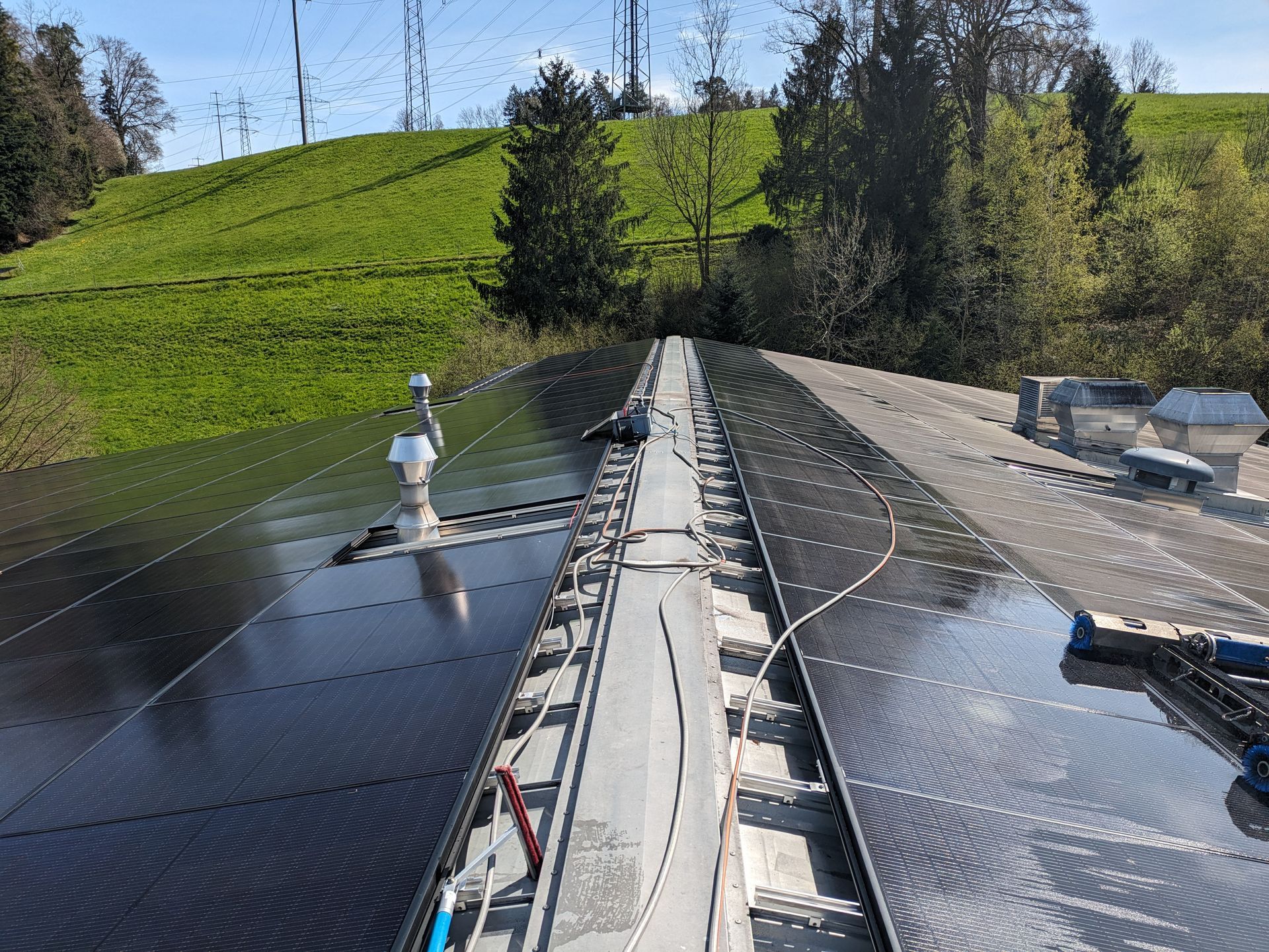 Solarpaneele auf einem Dach, im Hintergrund ein grasbewachsener Hügel. Strahlend sonniger Tag.