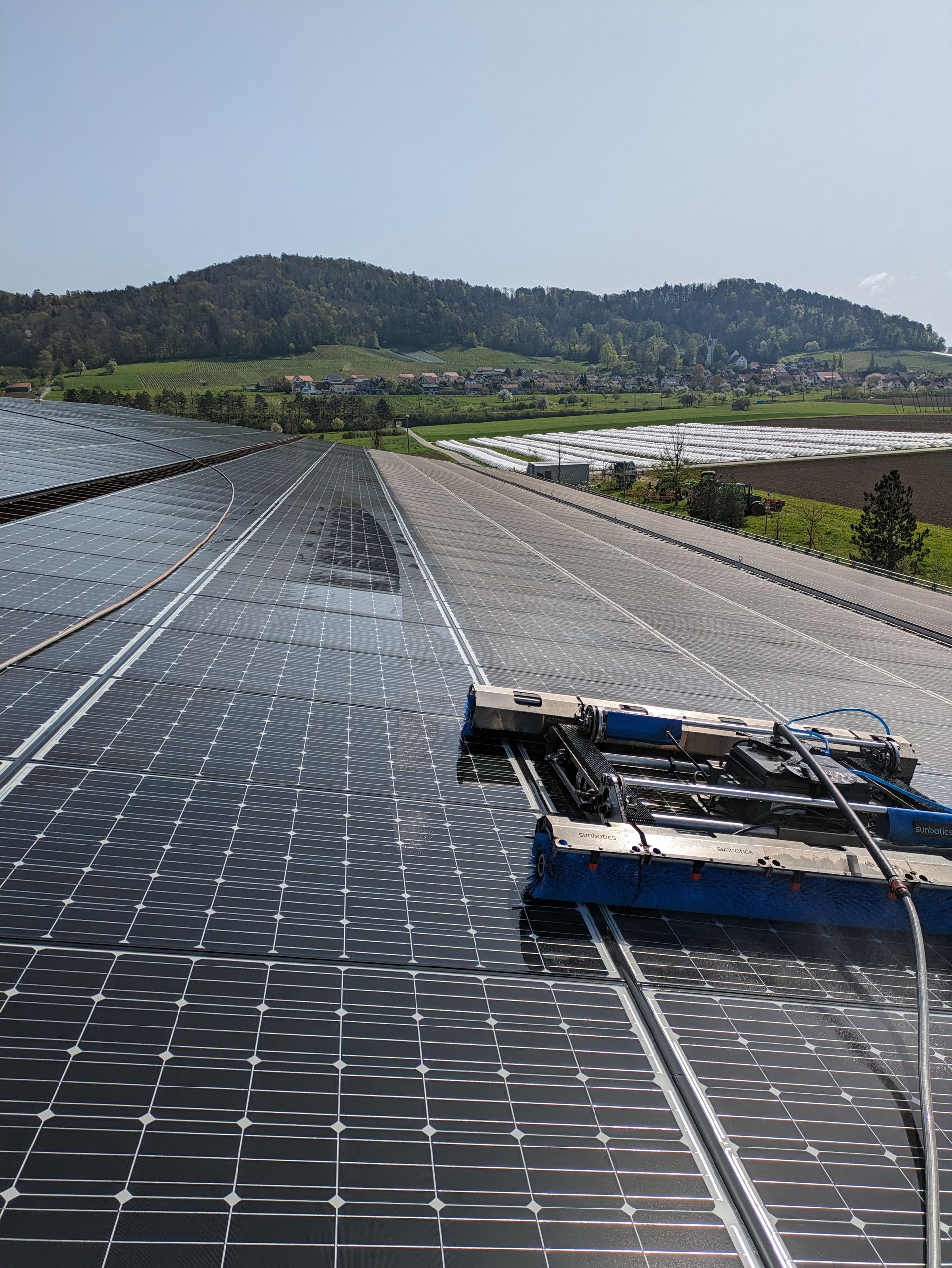Auf einem Dach werden Solarpaneele von einem blauen Reinigungsroboter gesäubert