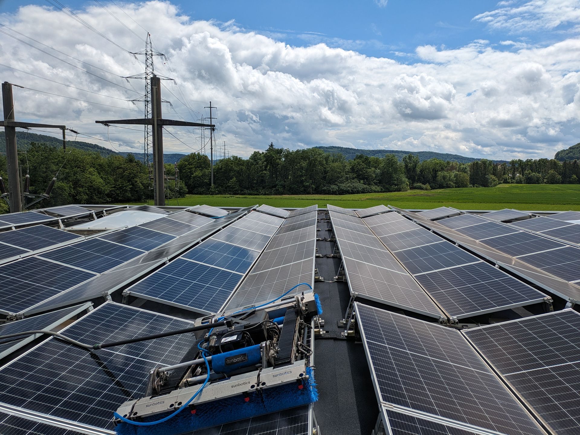 Auf einem Dach vor malerischer Kulisse wird eine Solaranlage von einem blauen Reinigungsroboter gesäubert.