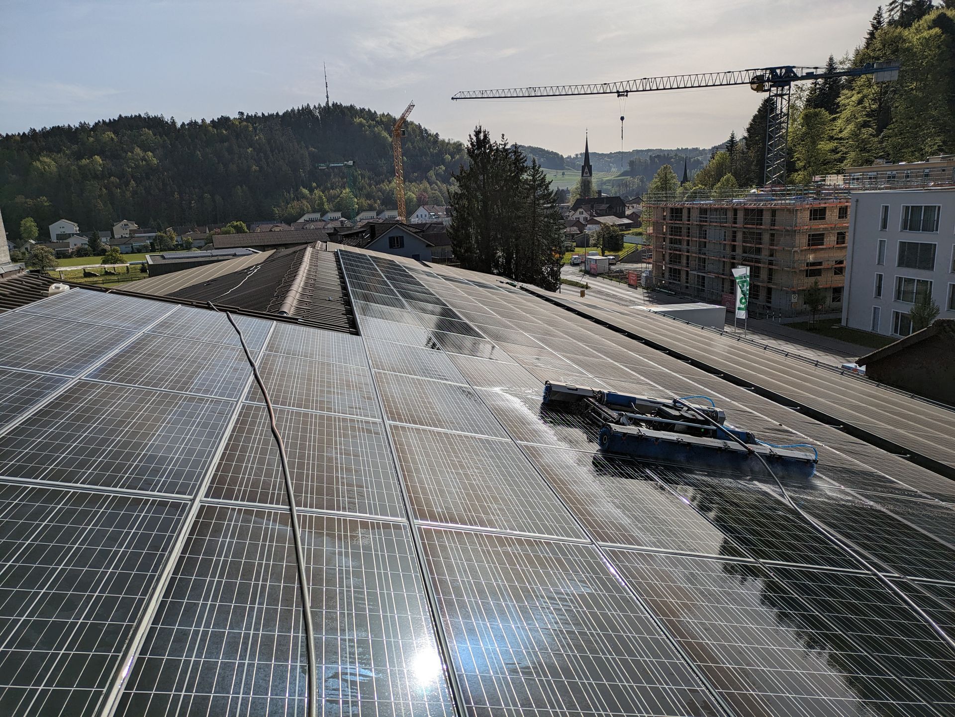 Auf einem Dach werden Solarpaneele gereinigt; im Hintergrund sind eine Stadt und Berge zu sehen.