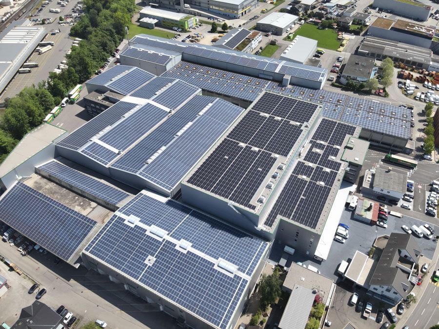 Luftaufnahme eines grossen Industriekomplexes, dessen Dach grösstenteils mit Solarmodulen bedeckt ist.
