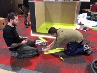 Deux hommes sont agenouillés sur le sol et travaillent sur un projet.