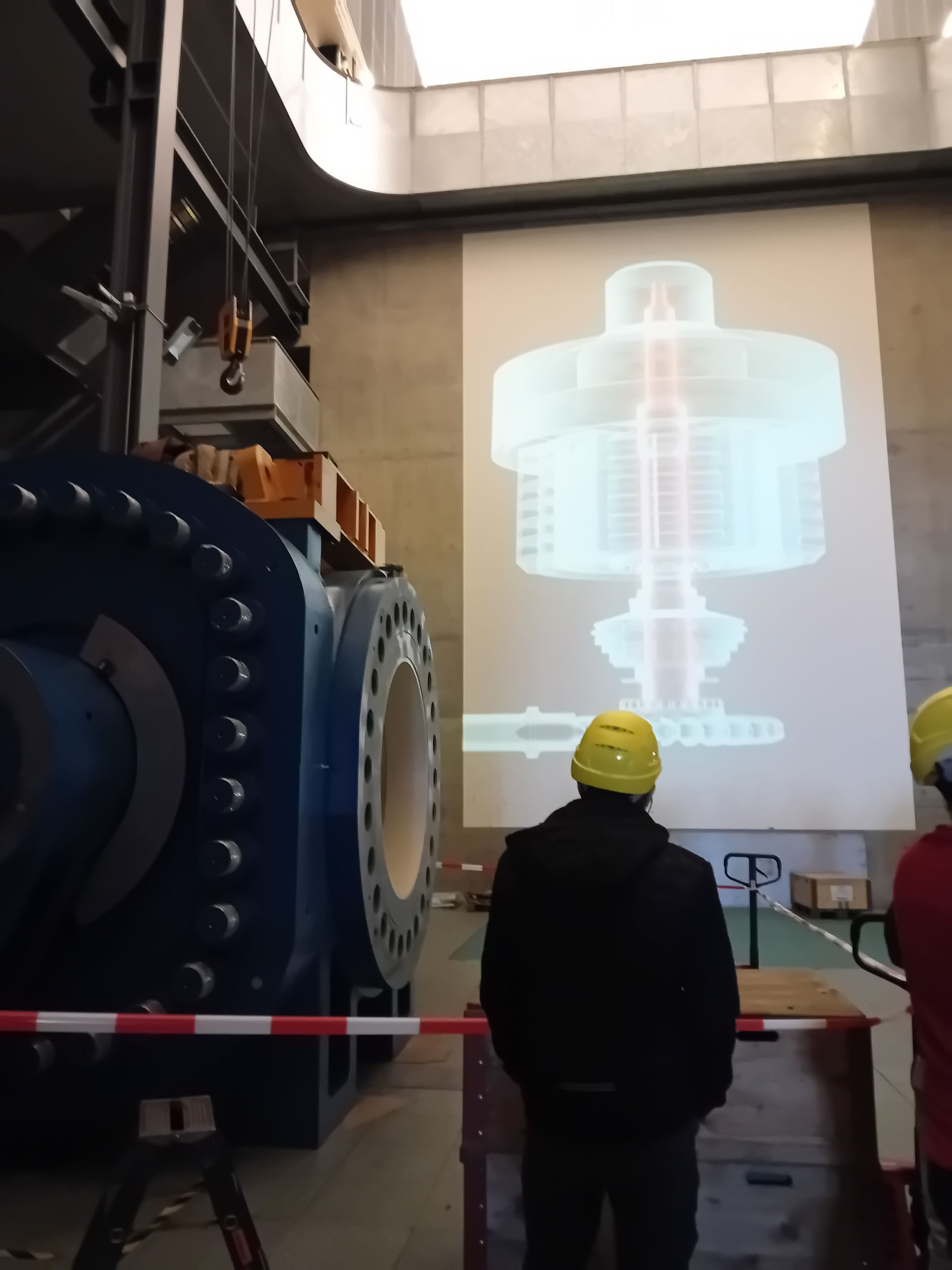 Un homme portant un casque jaune se tient devant une grande machine