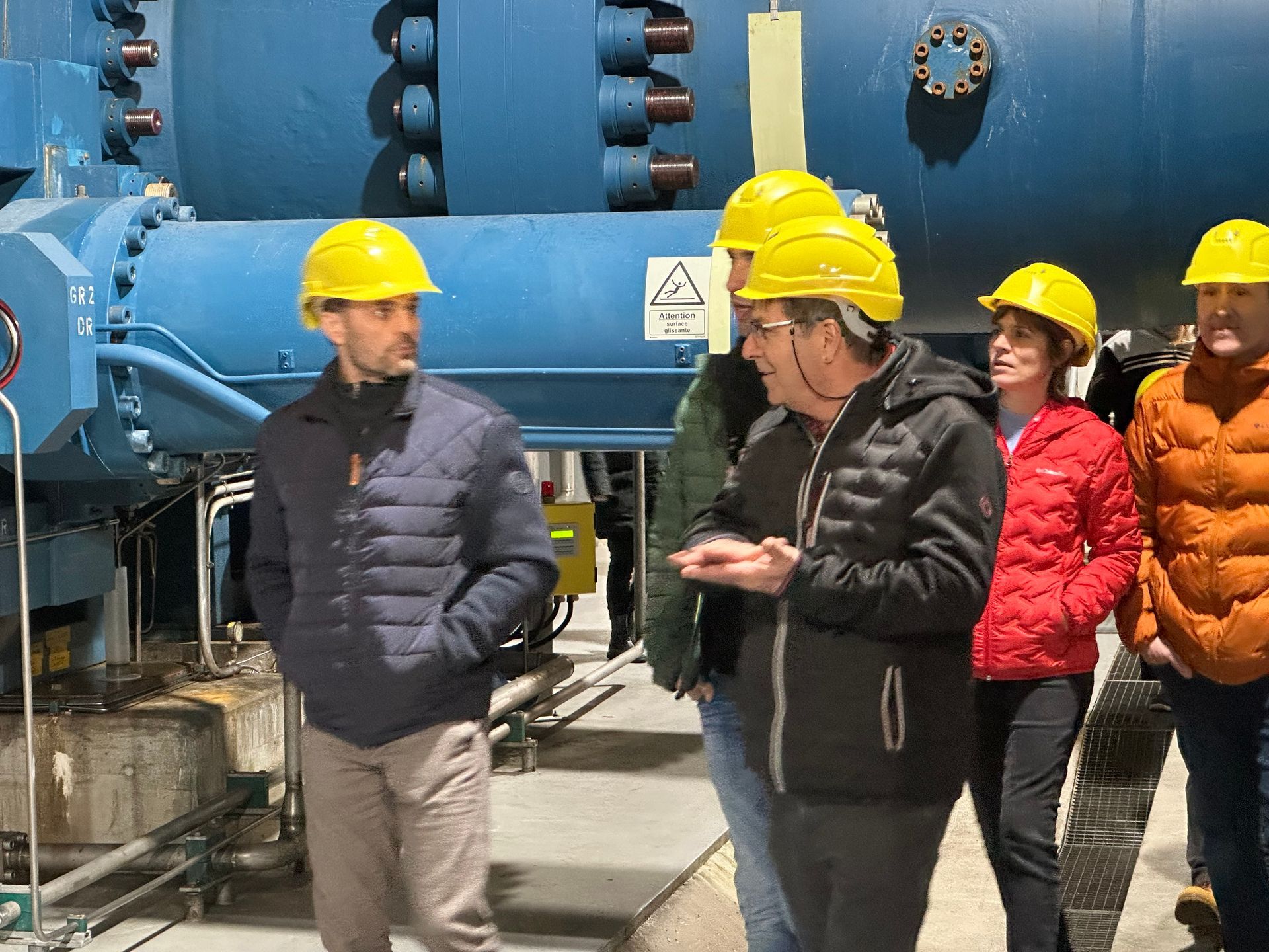 Un groupe de personnes portant des casques de sécurité se tient devant une machine bleue.