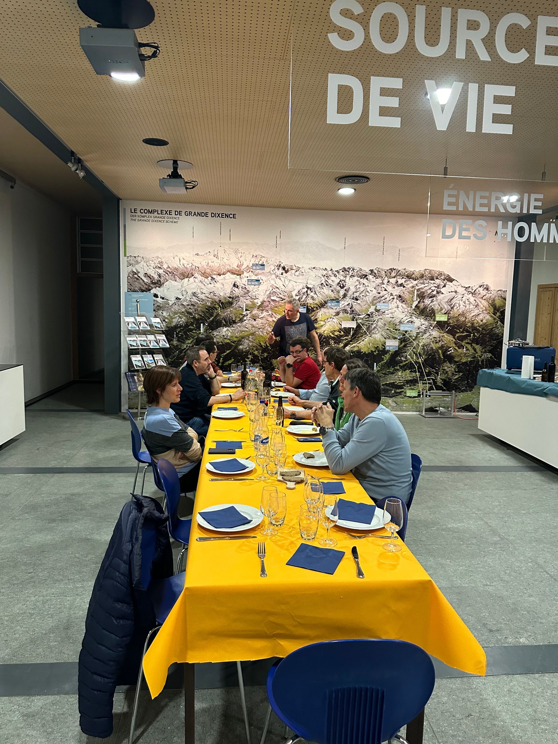 Un groupe de personnes est assis à une longue table devant un mur sur lequel est écrit source de vie