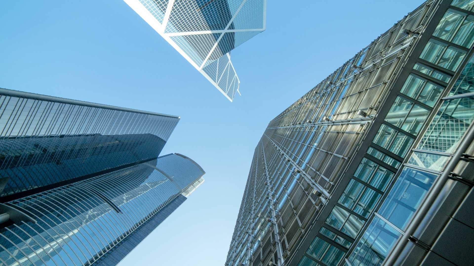 Skyscrapers viewed from below against a blue sky, with glass facades and one triangular building.