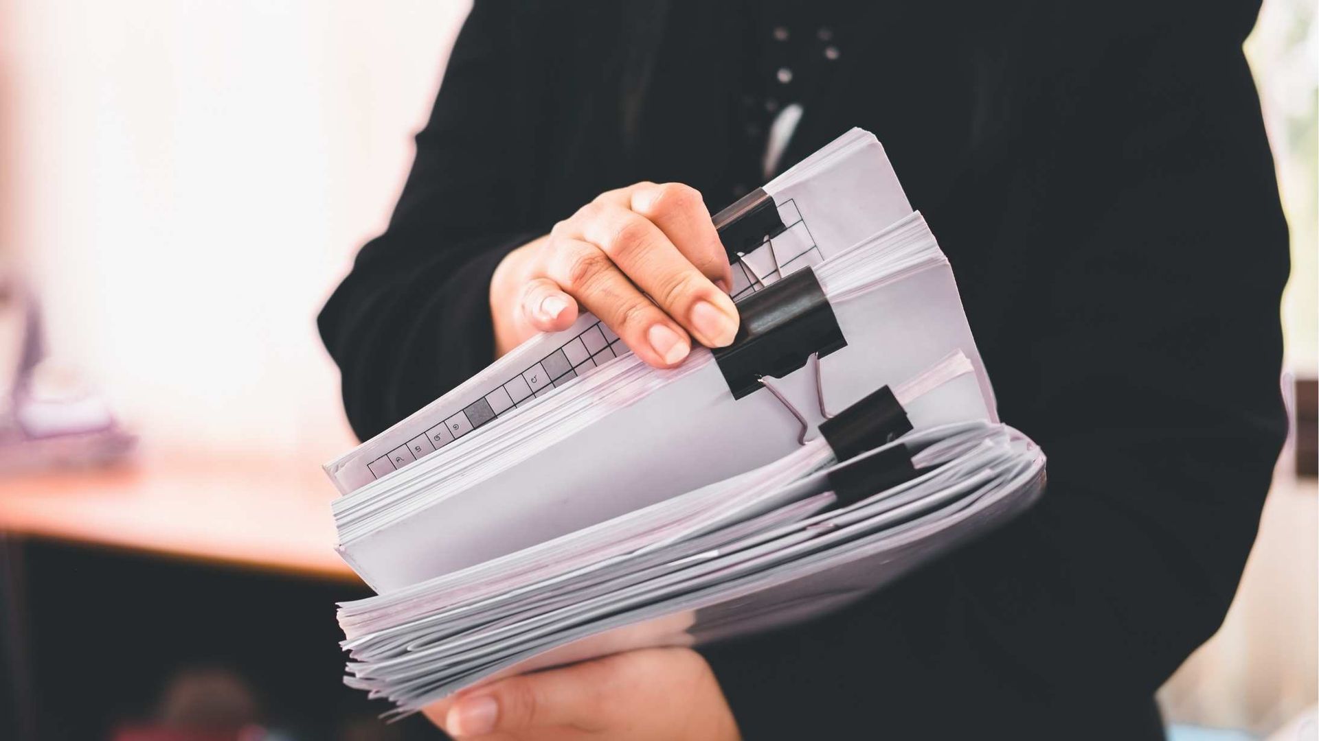 Person holding a stack of papers and folders in an office setting