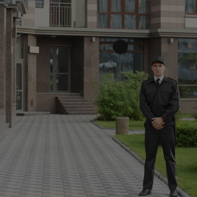 Guardia de seguridad con uniforme negro de pie frente a puertas de vidrio.