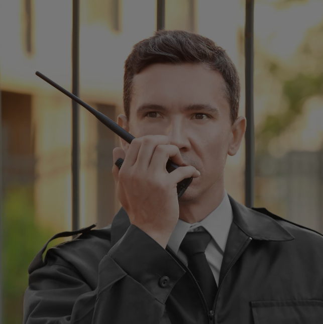 Guardia de seguridad con uniforme negro de pie frente a puertas de vidrio.