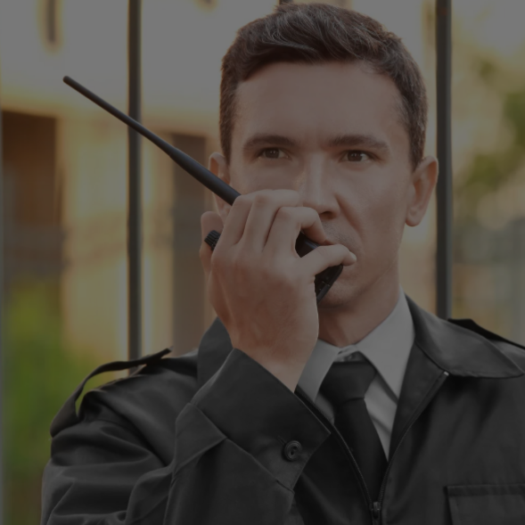 Guardia de seguridad con uniforme negro de pie frente a puertas de vidrio.