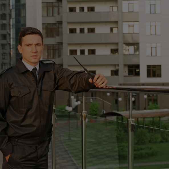 Guardia de seguridad con uniforme negro de pie frente a puertas de vidrio.