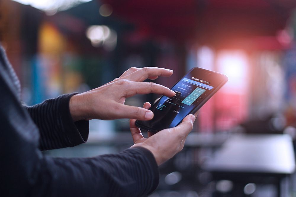 Close-up of hands using a smartphone screen displaying a data chart, with a blurred outdoor background.