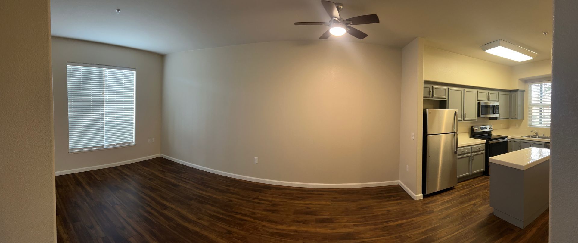 An empty room with a ceiling fan and a kitchen in the background.