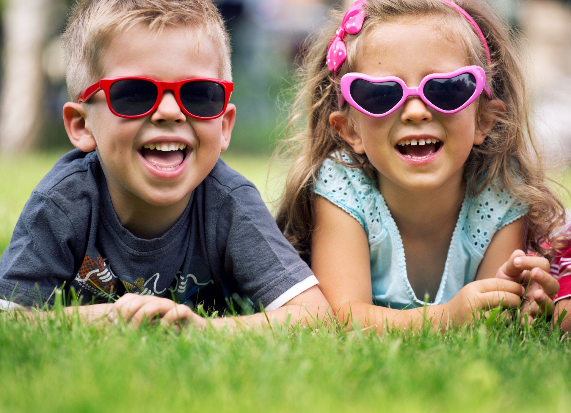A boy and a girl wearing sunglasses are laying in the grass.