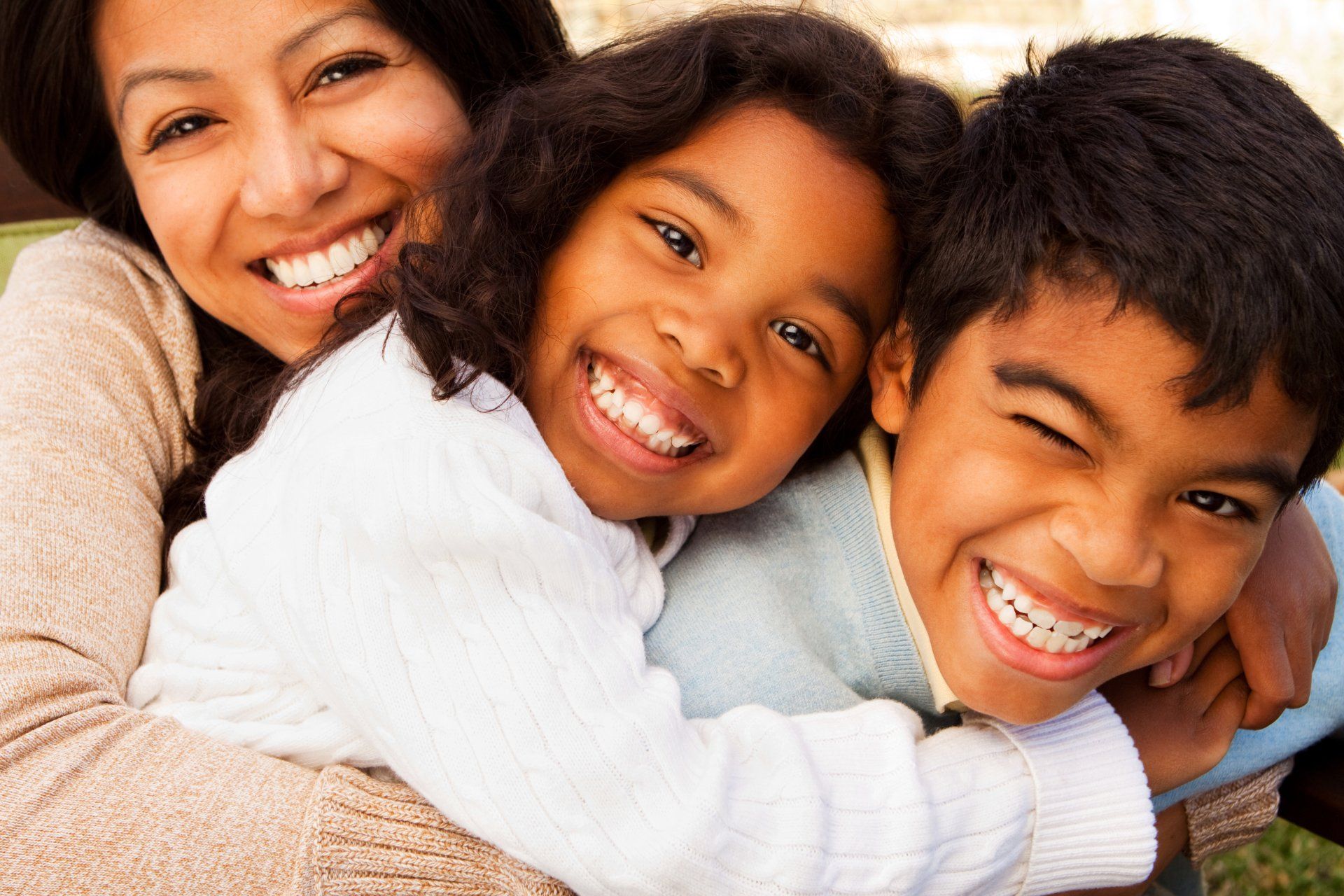 A woman is hugging two children who are smiling for the camera.