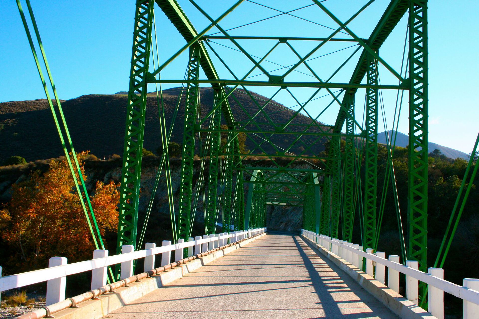 A green bridge with a white railing and mountains in the background