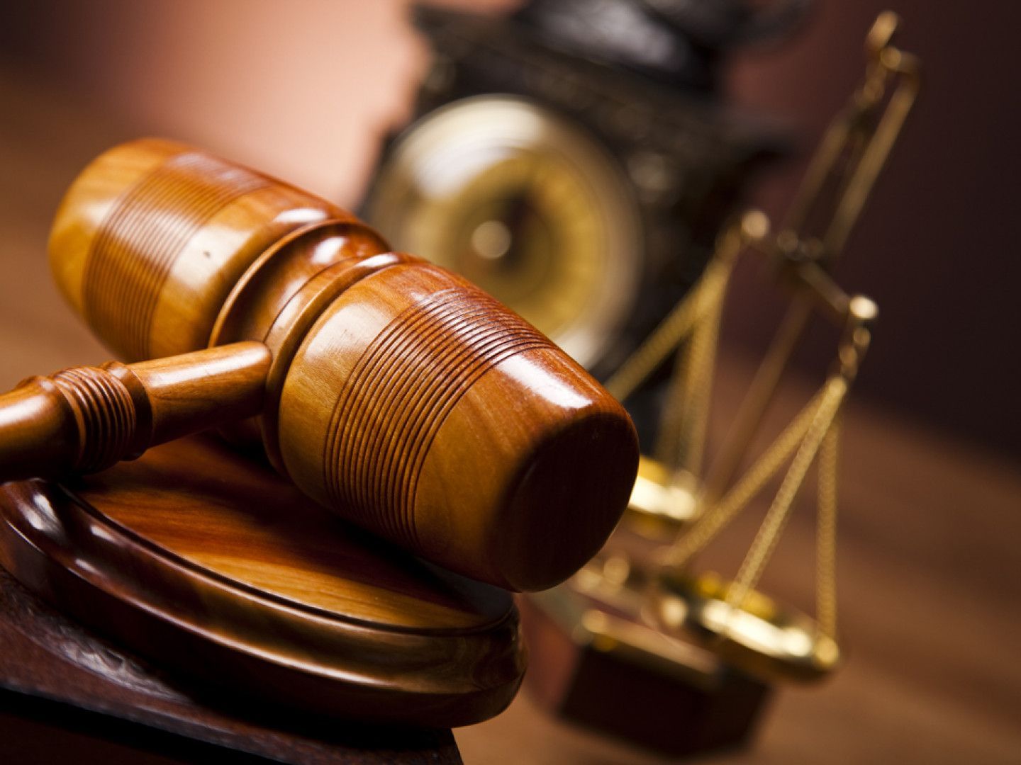 A wooden judge 's gavel and scales of justice on a wooden table.