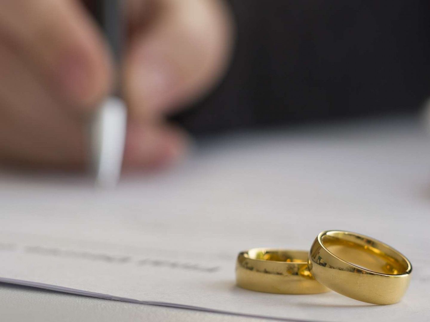 A person is writing on a piece of paper next to a pair of wedding rings.