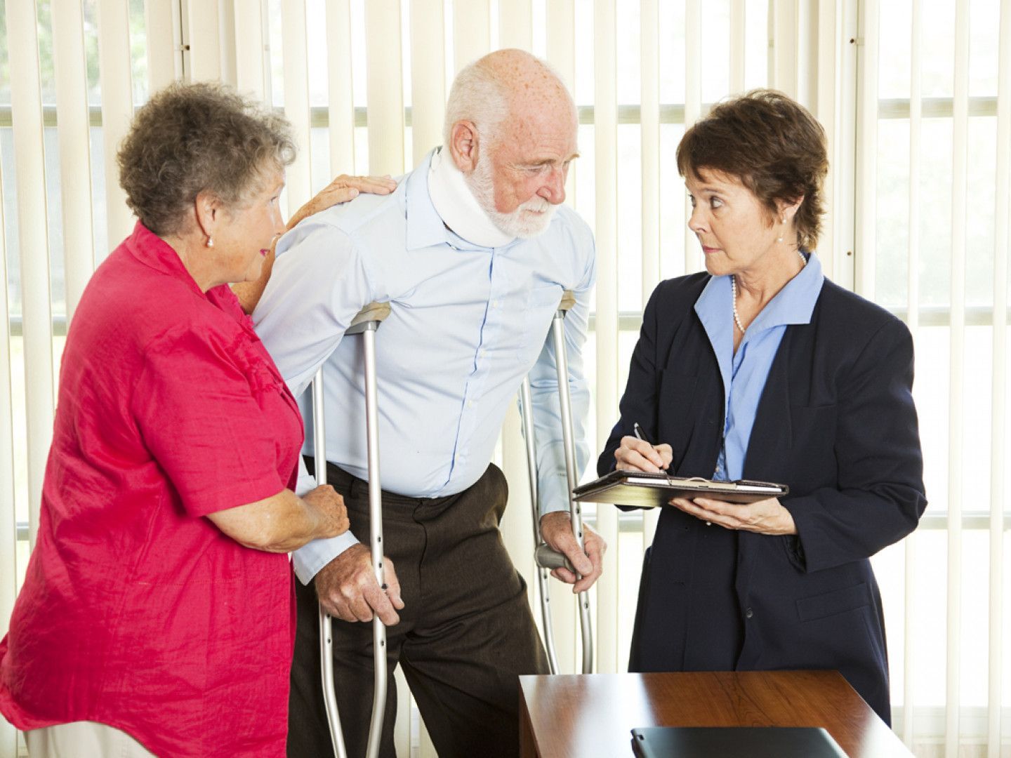 A man with crutches is talking to a woman and a woman is holding a clipboard.