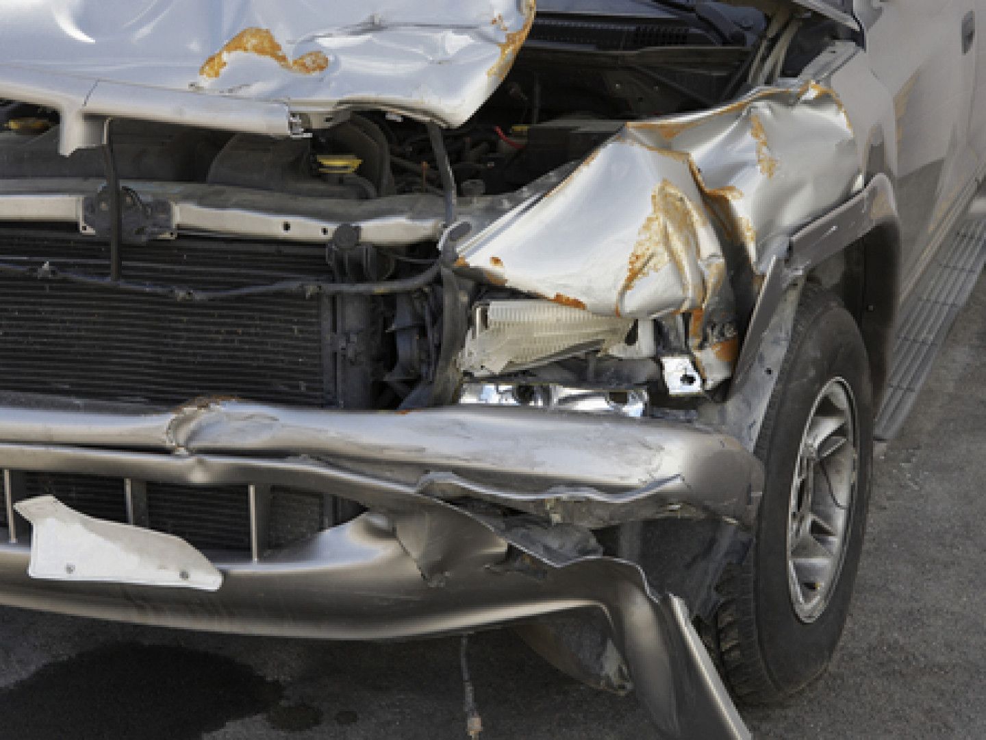 A silver truck with a damaged front end is parked on the side of the road.