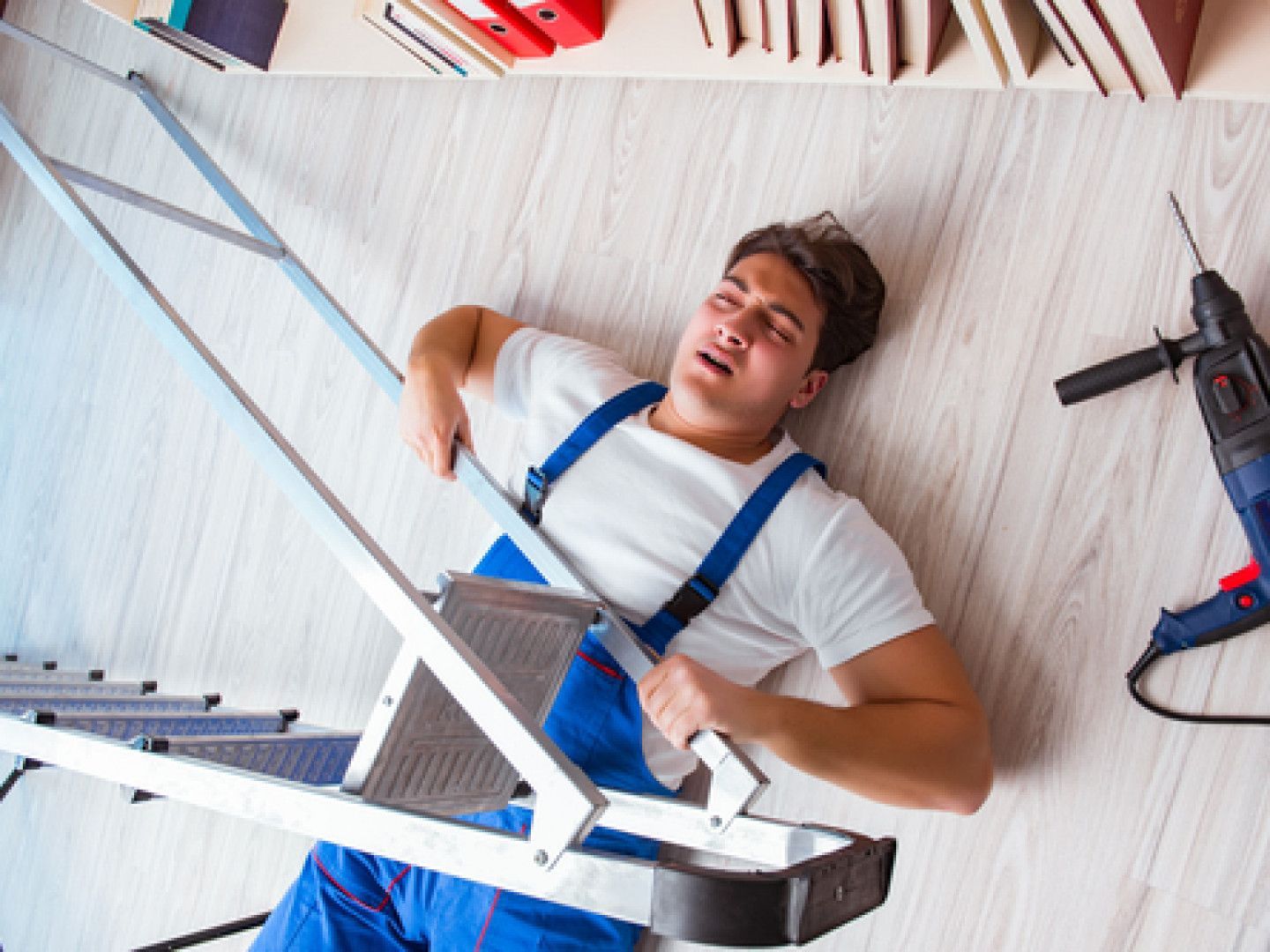 A man is laying on the floor after falling off a ladder.