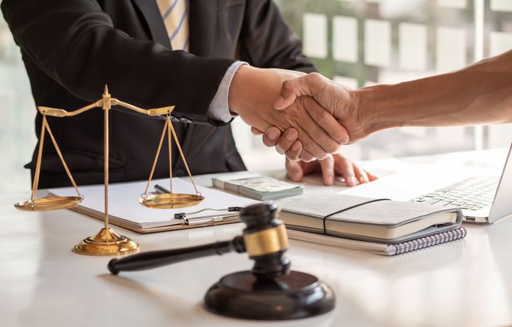 A lawyer is shaking hands with a client at a desk.