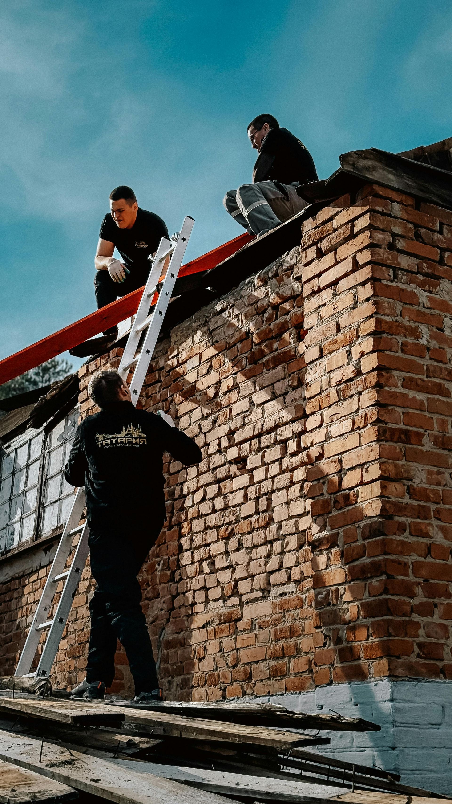 Gloved hand laying a red brick on a brick wall outdoors