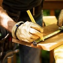 Gloved hands marking wood with a pencil and measuring tool on a workbench