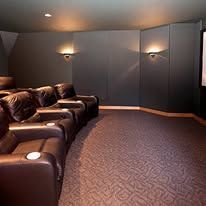 Dim home theater room with leather recliners, wall sconces, and patterned carpet