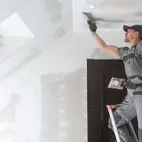 Worker painting a white ceiling indoors on a stepladder