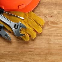 Work gloves, wrench, pliers, and screwdriver on a wooden surface