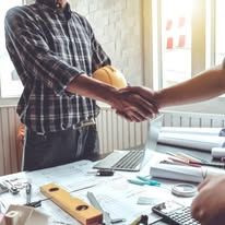 Two people shaking hands across a desk with papers, notebooks, and office supplies.
