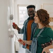 Two people holding screwdrivers and working on wall-mounted devices in a bright room