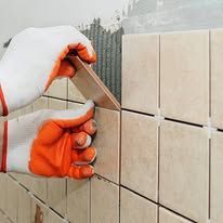 Gloved hands aligning beige wall tiles with a spacer during installation