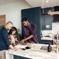 Three people review papers and a tablet on a kitchen island in a modern kitchen