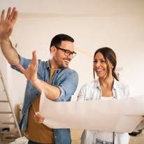 Two coworkers smiling and discussing a blueprint in an office setting