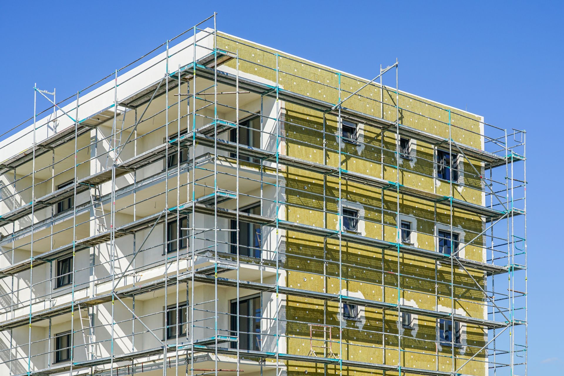 Apartment building under construction with scaffolding and yellow exterior panels