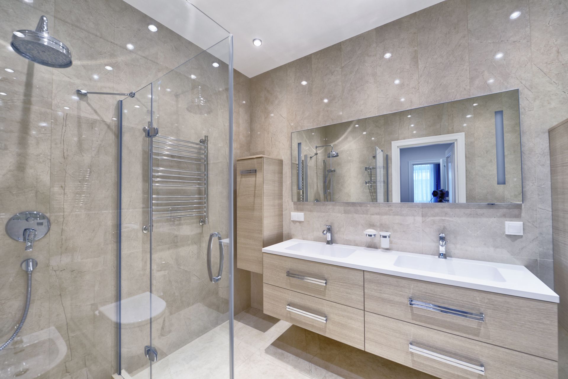 Modern beige bathroom with glass shower, towel warmer, double sink vanity, and large mirror