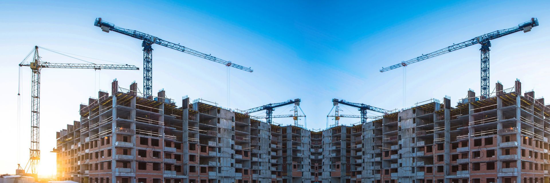 Large apartment buildings under construction with cranes against a clear blue sky at sunset