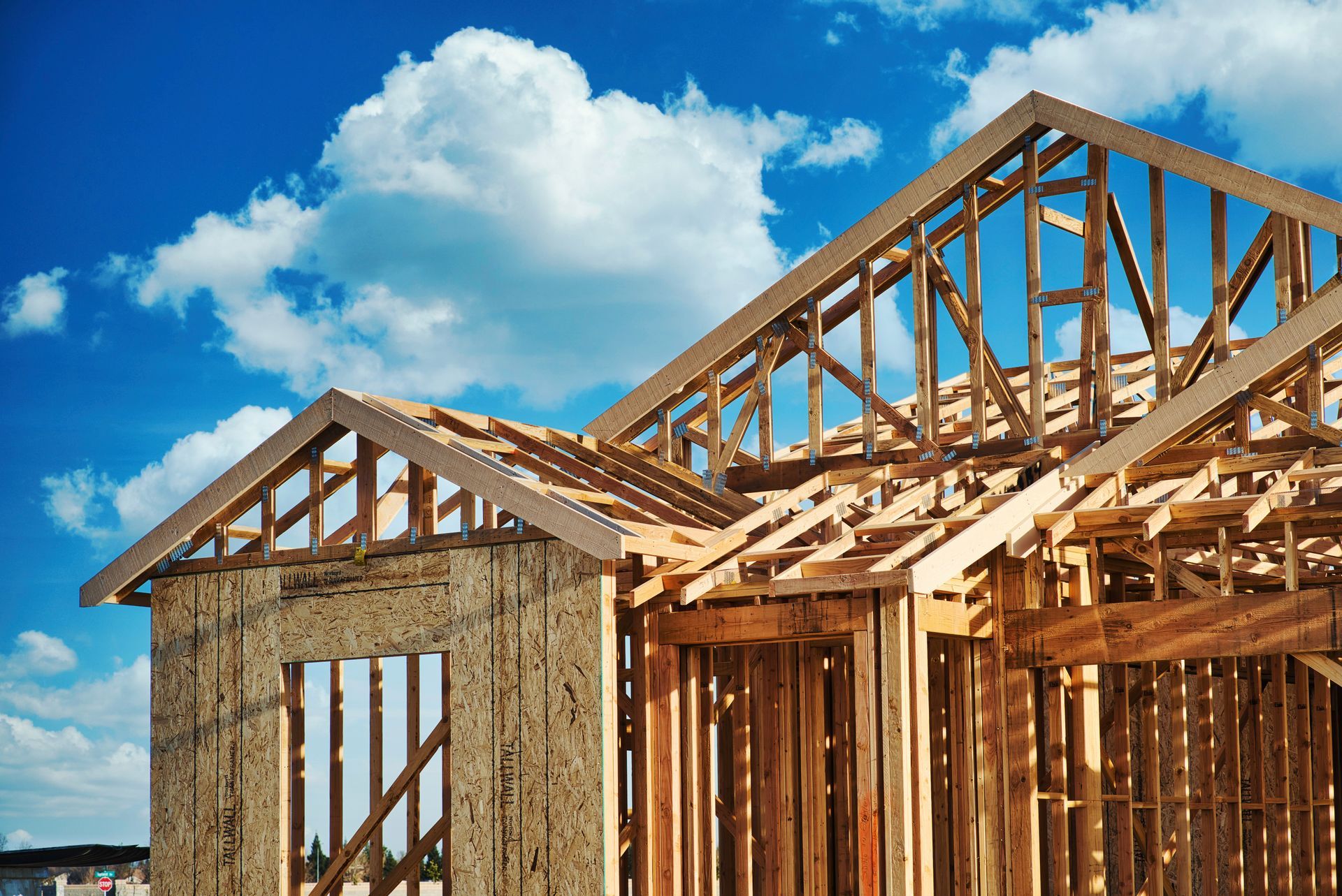 Wooden house frame under construction against a bright blue sky with clouds