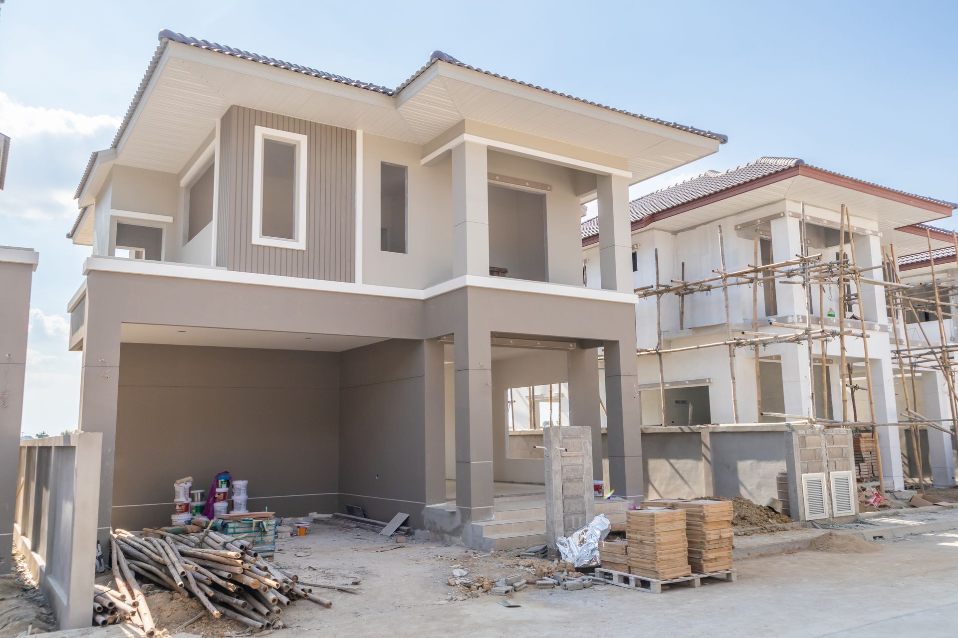 Two-story house under construction with unfinished exterior and building materials in the driveway
