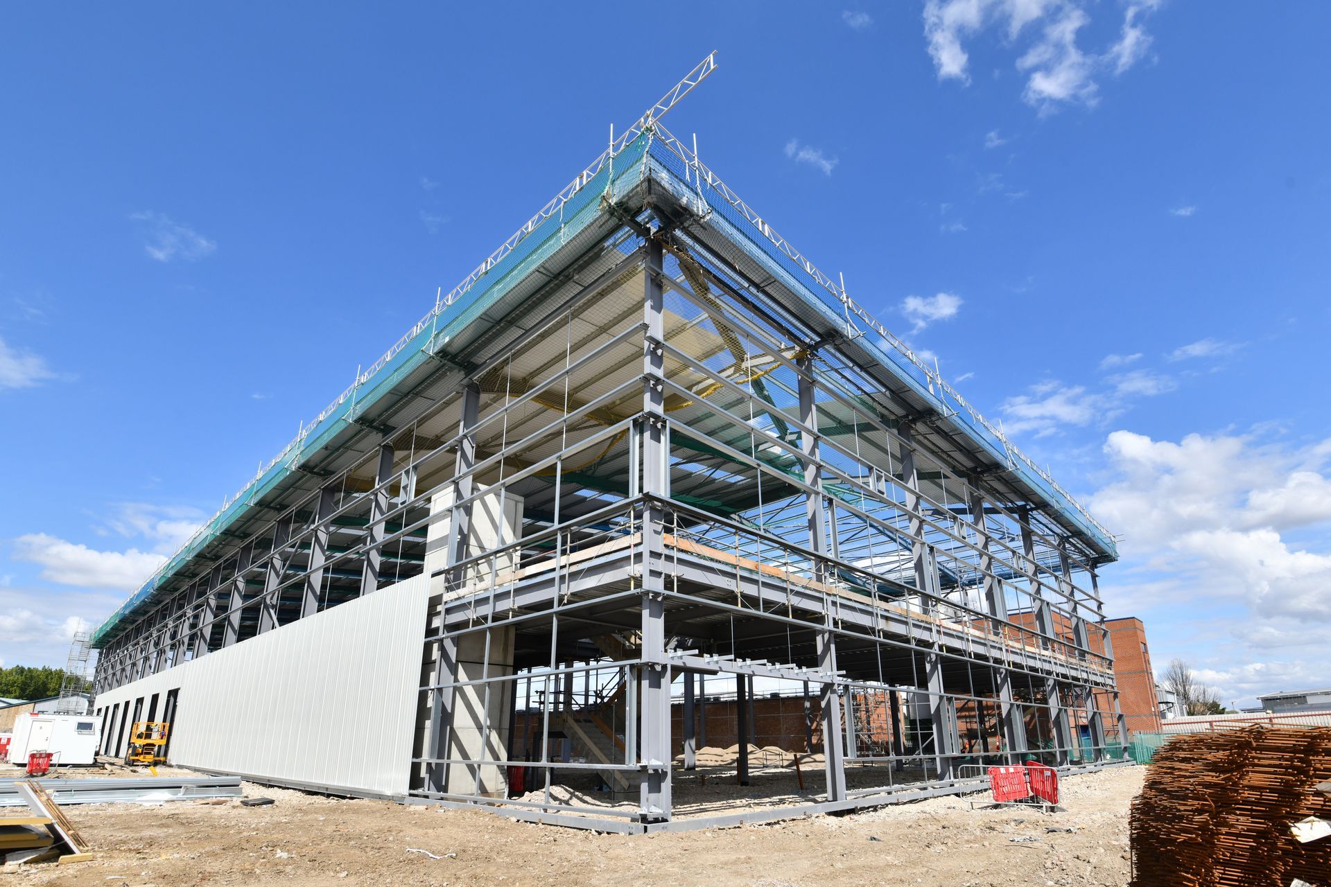 Steel-frame building under construction with scaffolding and a partly finished exterior under a blue sky