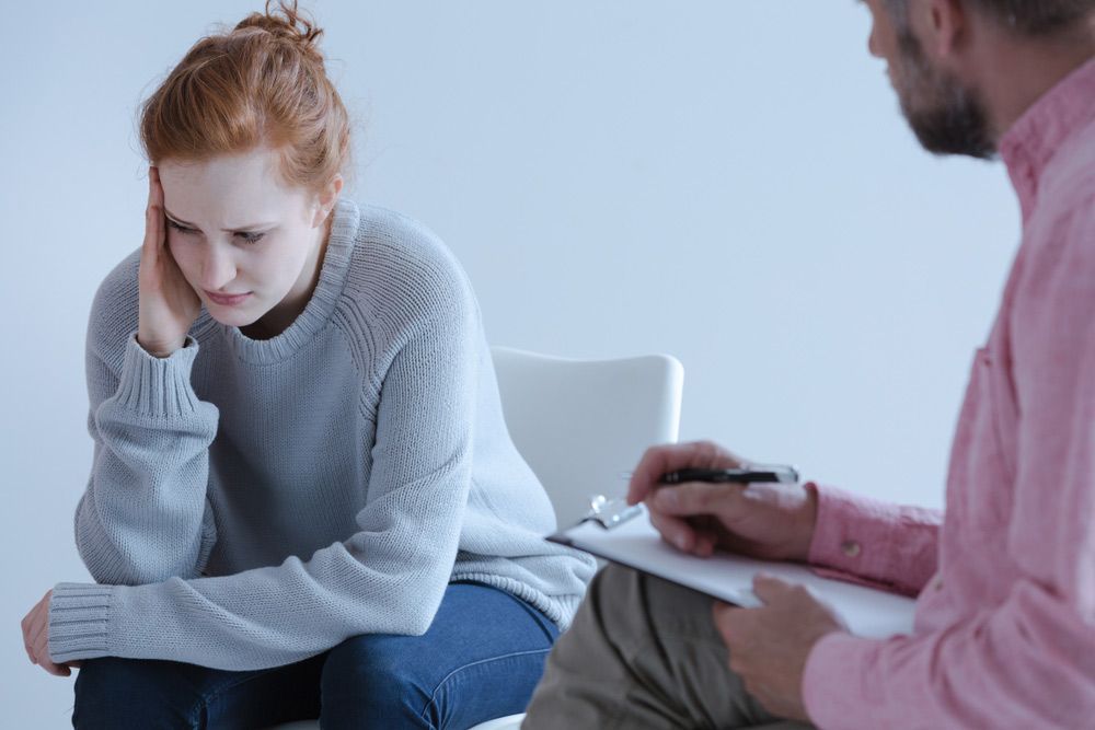 A Woman is Sitting in a Chair Talking to a Man in a Pink Shirt — Living Well Psychology Clinic in Erina, NSW