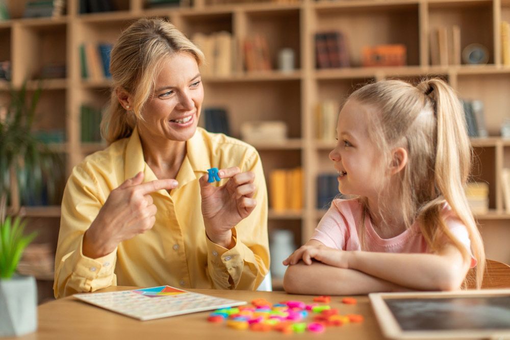A Woman is Teaching a Little Girl How to Play a Board Game — Living Well Psychology Clinic in Erina, NSW